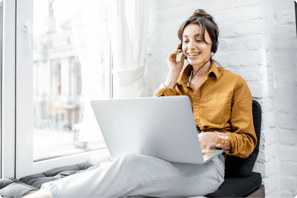 A woman sitting on a chair and talking on the phone while using her laptop.