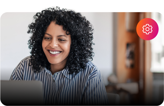 A woman with curly hair is smiling while using a laptop.
