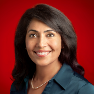 Portrait of a smiling woman with shoulder-length black hair wearing a blue shirt against a better experiences red background.