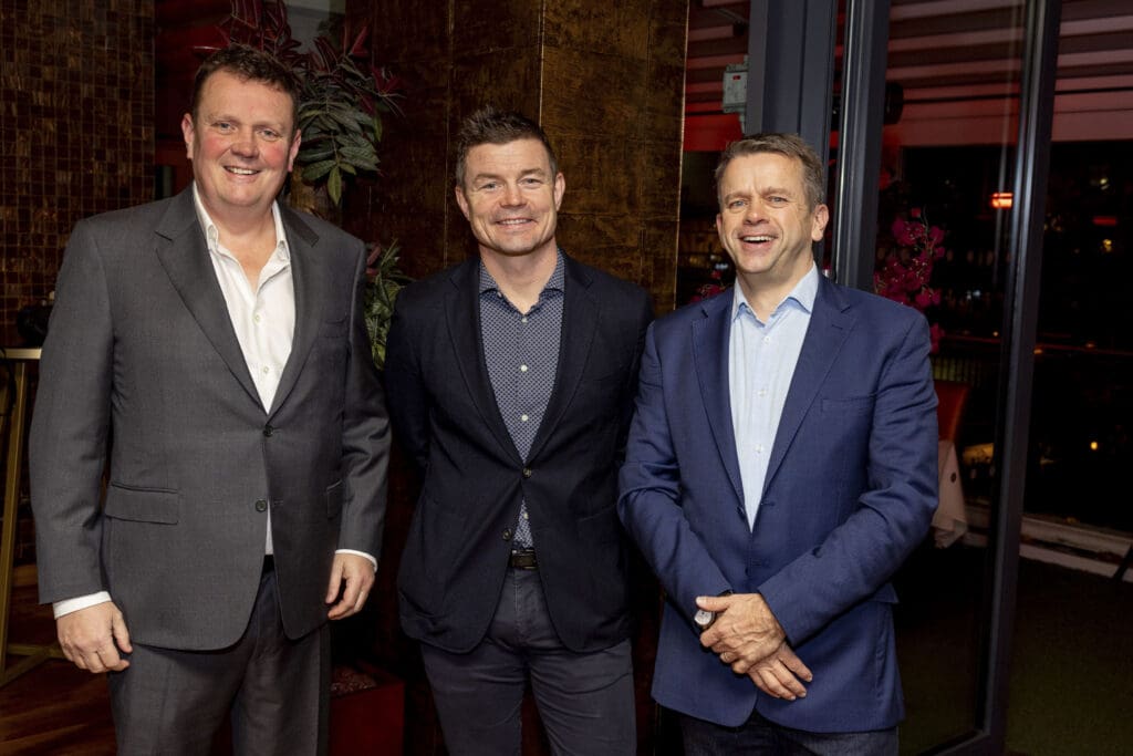 Three smiling men standing together indoors, two wearing suits and one in a casual blazer, posing for a photo at a Workair PR event.